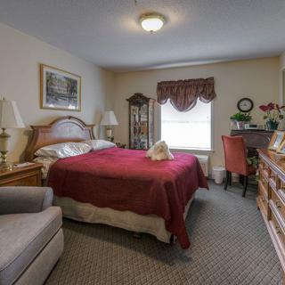 A cozy, traditionally decorated bedroom featuring a queen-sized bed with red bedding, an armchair, and a dresser.
