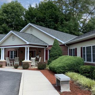 A suburban residential house with a porch, surrounded by trees and well-maintained landscaping.
