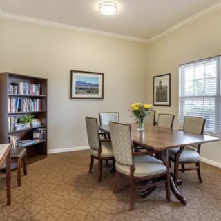 A cozy dining area with a wooden table, chairs, bookshelf, and large window.