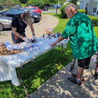 Two individuals interacting at an outdoor table during a community event on a sunny day.
