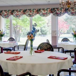 A well-lit dining area with round tables, decorated with flowers and set for a meal.