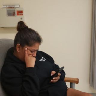 A person sitting in a hospital room, absorbed in their phone while deep in thought.