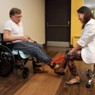 A healthcare professional assists a patient in a wheelchair with physical therapy exercises.