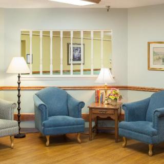 A cozy waiting room with blue sofa chairs, a coffee table, and floor lamps.