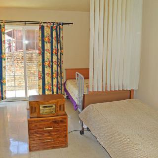 A bright room featuring a hospital bed, wooden furniture, and colorful curtains.