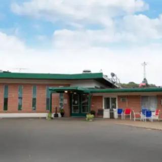 A brick building with a green roof and entrance, featuring chairs outside and a clear sky above.