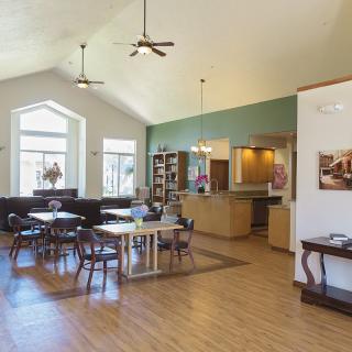 A spacious dining area with wooden tables and chairs, featuring large windows and ceiling fans.