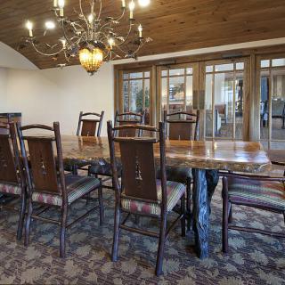A rustic dining room with a large wooden table and chairs, illuminated by an elegant chandelier.
