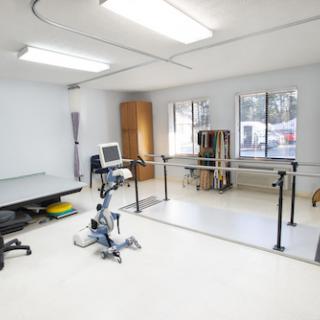 A spacious therapy room equipped with exercise equipment, including a bicycle and a ballet bar for rehabilitation sessions.