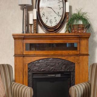A cozy living room setup featuring a wooden mantel with a large clock, candles, and a plant, flanked by two striped armchairs.