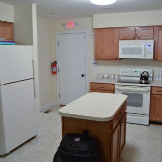 A modern kitchen with wooden cabinets, featuring a refrigerator, oven, microwave, and a central island.
