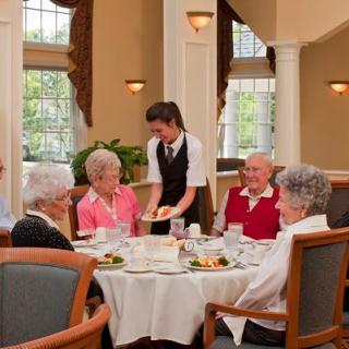 A group of elderly individuals enjoying a meal together while being served by waitstaff in a restaurant setting.