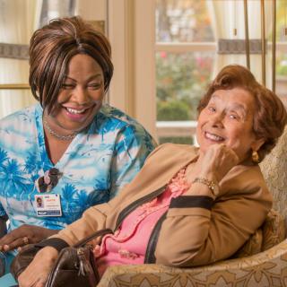 A caregiver shares a joyful moment with a senior woman in a cozy setting.