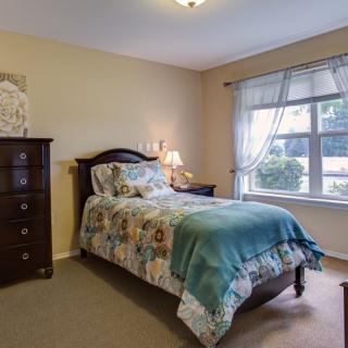 A cozy bedroom featuring a single bed with a colorful quilt, a wooden dresser, and a large window with curtains.