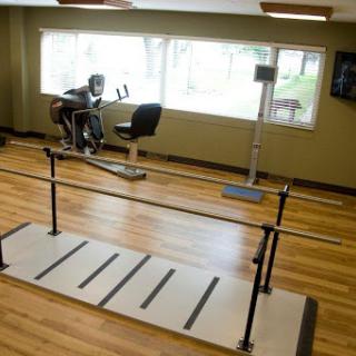 A view of a rehabilitation gym featuring exercise equipment, including a stationary bicycle and a barre for support.