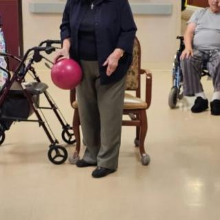 An elderly person holding a bowling ball, standing next to a walker.