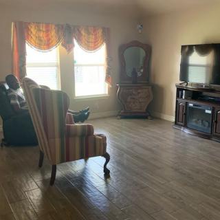A spacious living room with chairs, a television, and natural light streaming through the windows.