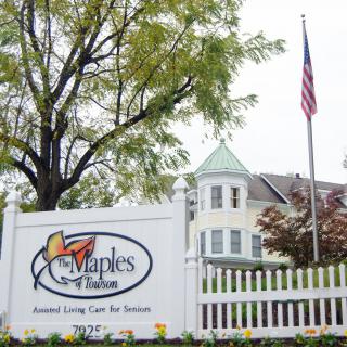 Sign for The Maples Retirement Community with building and American flag in the background.