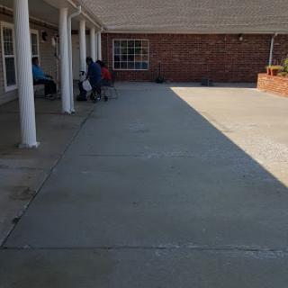 A view of a paved outdoor area beside a brick building, with people seated in the shade.