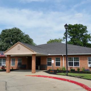 A brick building with a driveway and surrounding trees under a clear sky.