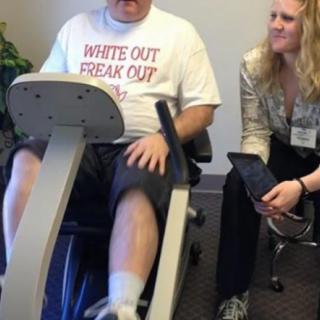 A person engages in physical therapy using a recumbent exercise bike, assisted by a healthcare professional.