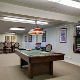 A well-lit billiard room with a pool table, framed pictures on the walls, and seating area.