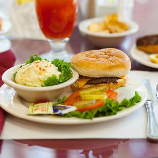 A meal consisting of a burger with a side of mashed potatoes and fresh salad on a dining table.