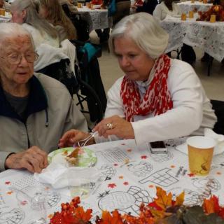 A person assisting an elderly individual during a community meal event.