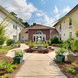 A landscaped courtyard with a central fountain and surrounding greenery leading to a building entrance.