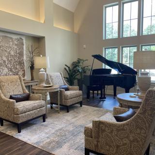 A cozy living room with armchairs, a coffee table, and a grand piano near large windows letting in natural light.