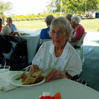 An elderly woman sitting at a table enjoying a meal outdoors.