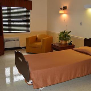 A clean and simple hospital room featuring a patient bed, an armchair, and natural light from the window.