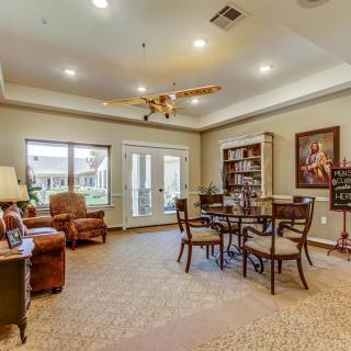A cozy living room featuring comfortable seating, a central table with chairs, bookshelves, and decorative elements.