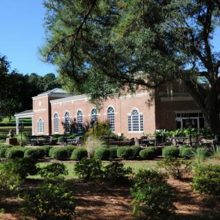 A beautiful brick building surrounded by a lush garden and trees on a sunny day.