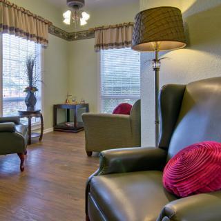 A cozy living room with comfortable armchairs, a floor lamp, and abundant natural light streaming through large windows.