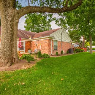 A brick house with a large tree and well-kept lawn in a suburban neighborhood.
