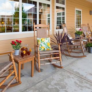 A cozy porch setup with rocking chairs, a small table with flowers and beverages, and decorative cushions.