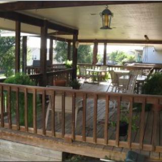 A cozy outdoor patio with a wooden deck, featuring tables and chairs surrounded by plants.