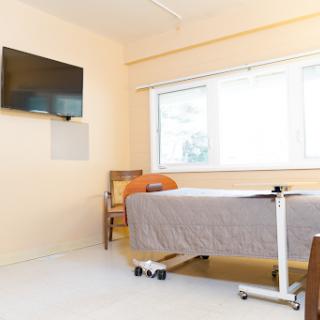 A neat and well-lit hospital room featuring a bed, a television, and a comfortable chair by the window.
