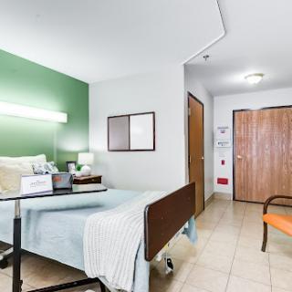 A well-lit hospital patient room featuring a bed, a chair, and essential medical furnishings.