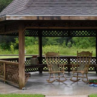 A wooden gazebo with rocking chairs in a garden setting.