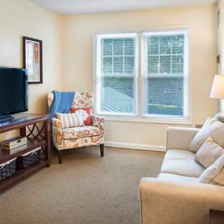A cozy living room with a sofa, armchair, television, and window allowing natural light.