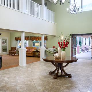 A spacious lobby featuring elegant interior design with a central round table adorned with flowers, surrounded by columns and a chandelier.