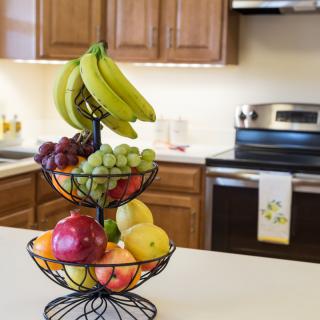 A well-organized fruit basket on a kitchen countertop, filled with bananas, grapes, apples, and lemons.