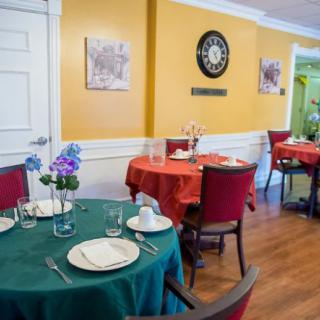 A cozy restaurant interior with round tables set for dining, adorned with colorful tablecloths and floral centerpieces.