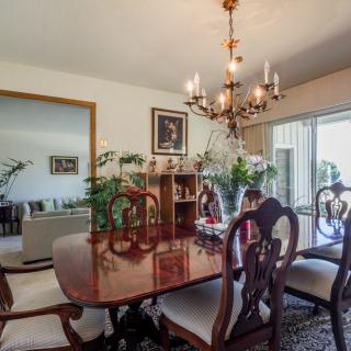 A cozy dining room with a wooden table and chairs, decorated with plants and illuminated by a chandelier.