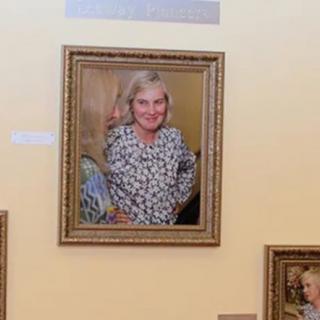 A framed portrait of a smiling individual displayed on a gallery wall.