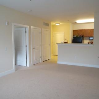 A spacious, empty apartment with an open floor plan and a view of the kitchen area.