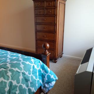 A cozy bedroom featuring a teal quilt, wooden dresser, and a space heater.