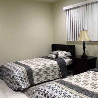 A bedroom with two neatly made twin beds, a bedside table with a lamp, and window blinds.